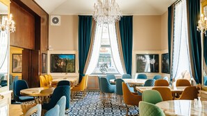 A dining area with round tables, blue and yellow chairs, a patterned floor, and a chandelier. - Hotel Praga 1885 (Prague)