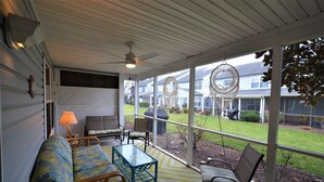 Een overdekt terras met een bank, stoelen en een tafel.
