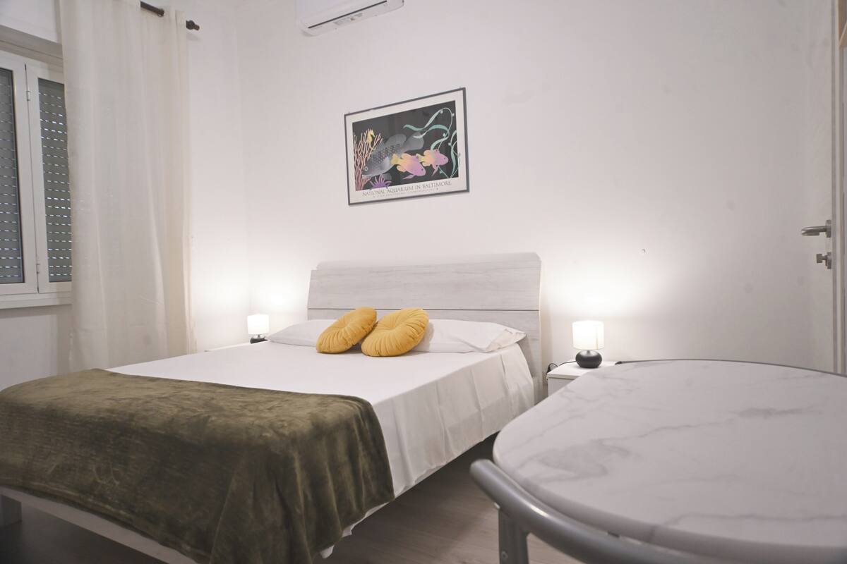 Een slaapkamer met een bed, bedlampen, een ronde tafel en een aan de muur hangend schilderij.
