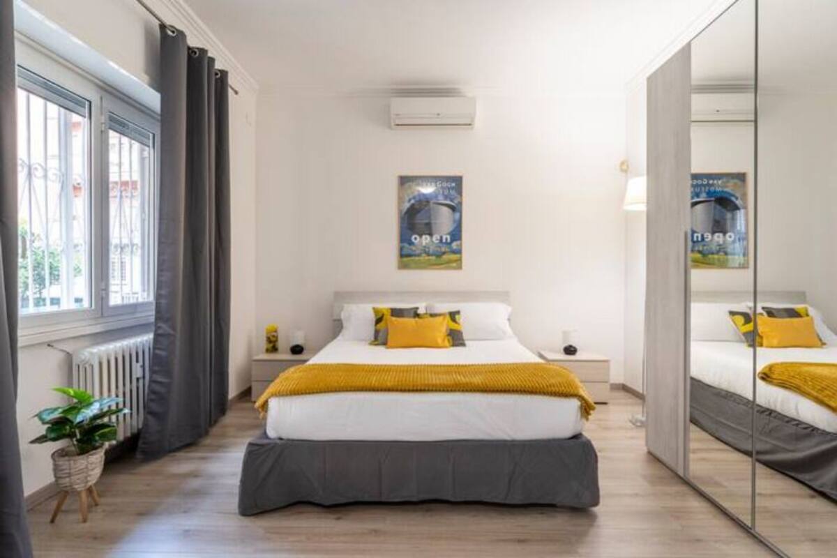 Een moderne slaapkamer met een groot bed, een nachtkastje, een spiegel en een raam met gordijnen.