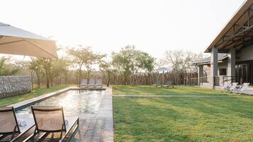 A poolside area with lounge chairs, a stone wall, and a building with a modern design.
