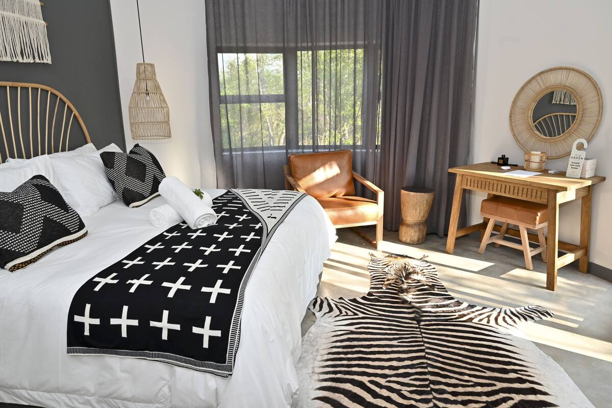 A bedroom with a bed, a chair, a desk, and a window with curtains.