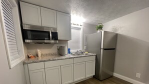 A compact kitchen with white cabinets, a stainless steel refrigerator, and a microwave.