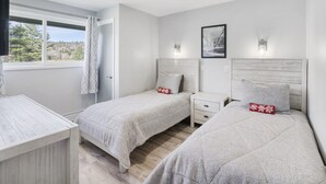 Un dormitorio con dos camas, una mesita de noche y un ventanal con vistas a árboles.