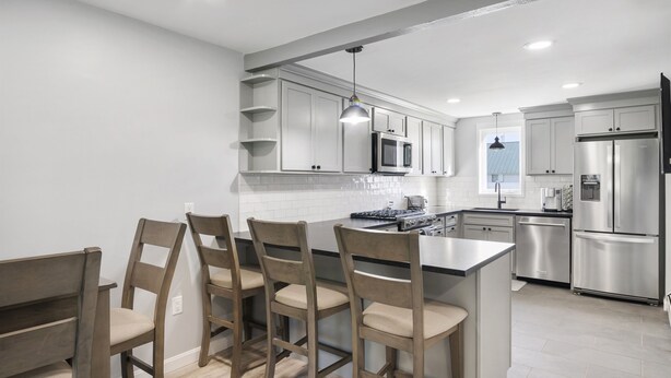 Una cocina moderna con armarios blancos, electrodomésticos de acero inoxidable y una isla central con taburetes de bar.