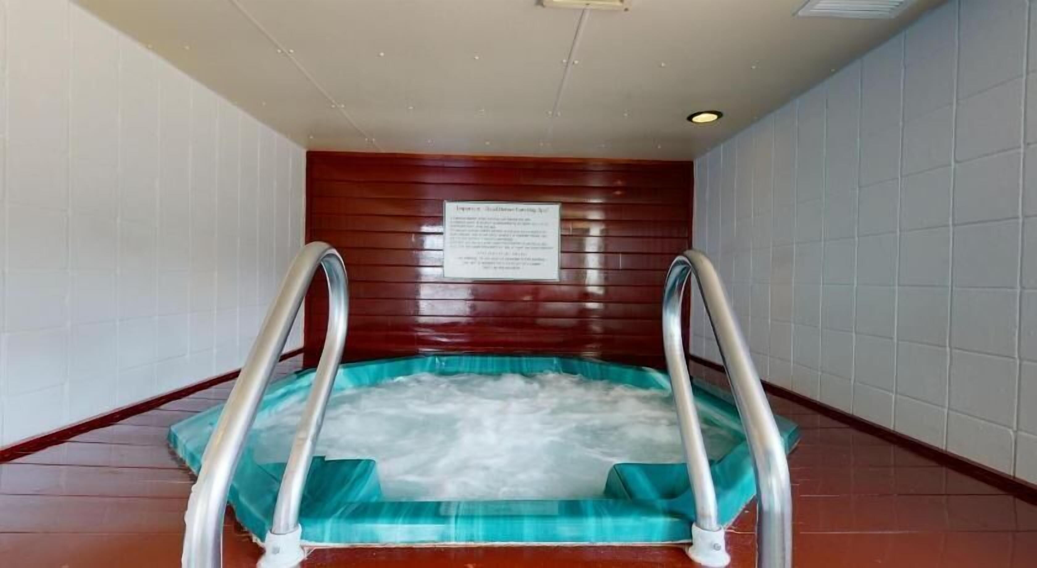 Un bain à remous doté de barrières métalliques, entouré de murs carrelés et de panneaux en bois.
