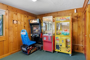 A room with wooden walls, a blue arcade racing game, a claw machine, and a yellow taxi-themed game. - 2 BR Village Green, Rec Path! Fantastic Location! (Stowe)