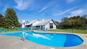 Una piscina con sillas de descanso, una casa de fachada blanca y un césped verde.