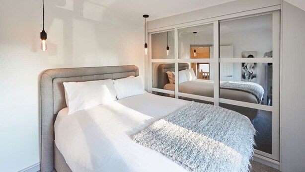 Une chambre moderne avec un grand lit, une armoire intégrée et des luminaires suspendus.