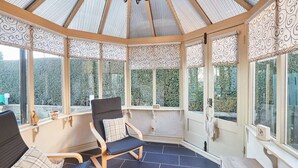 Une véranda dotée d’un plafond incurvé, de deux fauteuils avec des coussins et offrant une vue sur la verdure environnante.