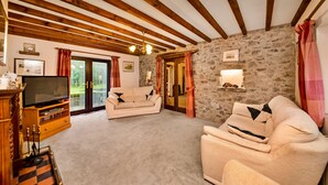 Uma sala de estar acolhedora com parede de pedra, vigas de madeira, televisão e sofá.