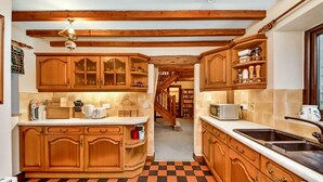 Uma cozinha com armários de madeira, piso xadrez e escada que leva a outro cômodo.