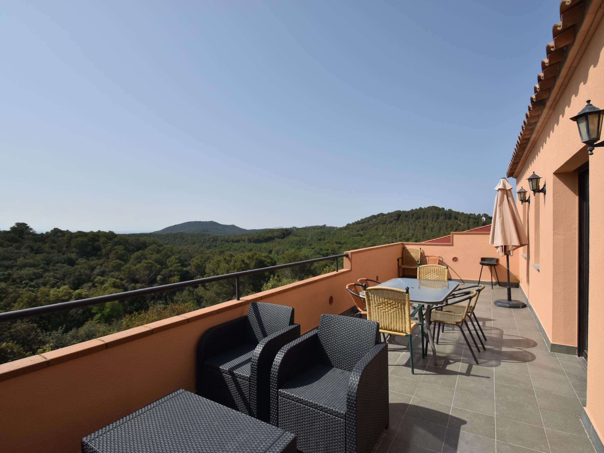 A balcony with wicker furniture, a table, and a view of a forested hill.