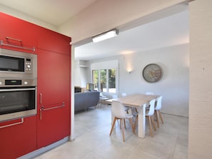 A modern kitchen with red cabinets and stainless steel appliances, a dining area with a wooden table and white chairs, and a large window providing natural light.