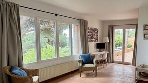 Una habitación con cama, una silla, una mesa y vistas al verde exterior.