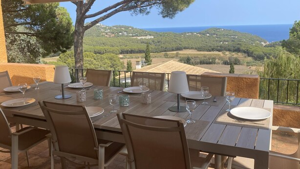 Un comedor al aire libre con una mesa preparada para cuatro, con vistas panorámicas al mar y las colinas.