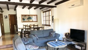 A living room with a sofa, a TV, and a dining area with chairs and a table. - Casa Pollo (Begur) (Begur)