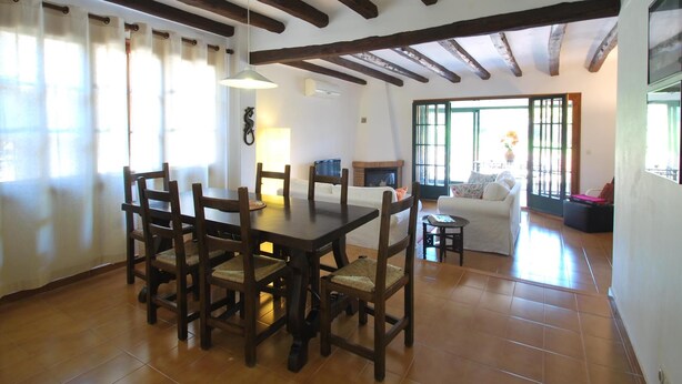 A dining area with a wooden table and chairs, a fireplace, and a sofa in the background. - Casa Pollo (Begur) (Begur)