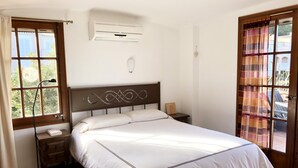 A bedroom with a bed, bedside table, lamp, air conditioning unit, and a view of the outdoors through a window. - Casa Pollo (Begur) (Begur)