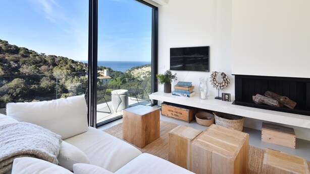 A modern living room with a large window, a fireplace, and a view of the sea. - Villa Energias Serenas (Begur, Sa Riera) (Begur)