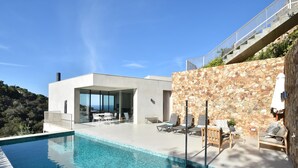 A modern poolside area with a clear blue pool, stone wall, and outdoor seating. - Villa Energias Serenas (Begur, Sa Riera) (Begur)