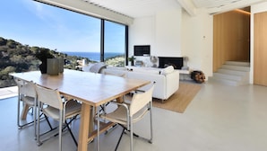 A modern living room with a large window offering a view of the sea, a fireplace, and a staircase leading to another level. - Villa Energias Serenas (Begur, Sa Riera) (Begur)