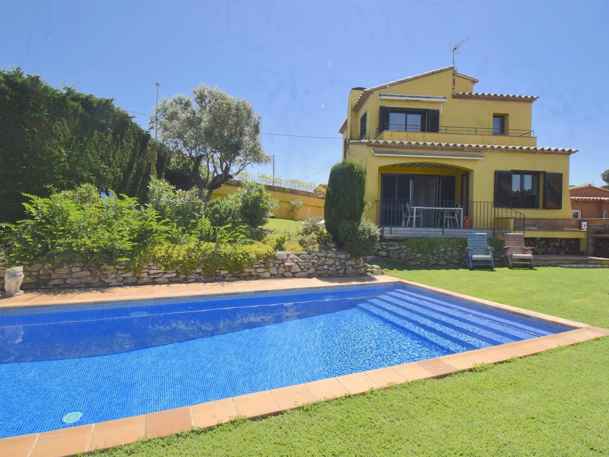 A two-story yellow house with a swimming pool in front.