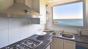 A kitchen with a gas stove, a stainless steel range hood, a double sink, and a window with a view of the ocean. - Apartament Catalonia (Begur, Sa Riera) (Begur)