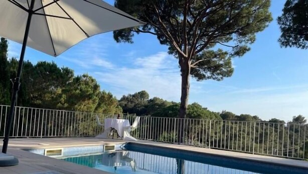 A swimming pool with a white umbrella, surrounded by a metal fence and trees. - Casa Bosc (Begur) (Begur)