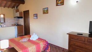 A bedroom with a bed, a dresser, a TV, and a small kitchen area. - Studio apartment in farmhouse with wine production (Toscana)