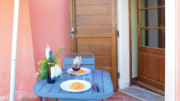 A table set with a bottle of wine, glasses, and a plate of spaghetti under a colorful umbrella. - Studio apartment in farmhouse with wine production (Toscana)