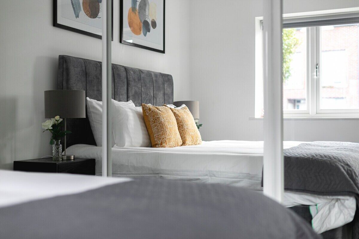 A bedroom with a grey upholstered headboard, white bedding, and two decorative pillows.