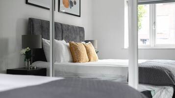 A bedroom with a grey upholstered headboard, white bedding, and two decorative pillows.