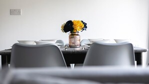 Una mesa de comedor con un florero, sillas blancas y un cuadro en la pared.