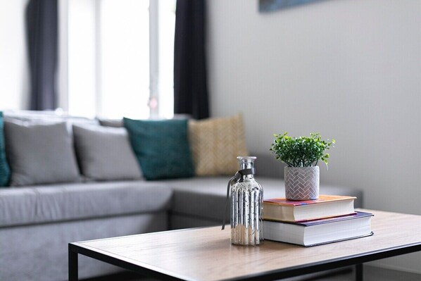 En moderne stue med en grå sofa, et sofabord, en dekorativ flaske, en potteplante og en stabel bøger.