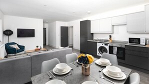 Una cocina moderna con lavadora y microondas integrados, un comedor con mobiliario gris y un televisor de pantalla plana montado en la pared.