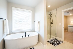 Bathroom features a bathtub, glass-enclosed shower, and window with blinds.