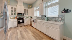 A modern kitchen with white cabinetry, a microwave, an oven, and a dishwasher. There is a window with blinds and a sign indicating a coffee shop. - The Tipsy Turtle features a playroom for little ones, an arcade game room for bi (Port Aransas)