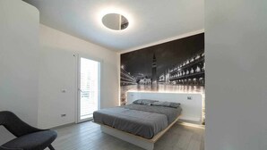 A modern bedroom with a bed, a chair, and a cityscape mural on the wall. - Residence Arena - new, modern, air con and pool (Lazise)