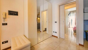 A hotel room with a large mirror, a bedside table, and a view into the kitchen. - Residence Moky D14 - pool, private garden, garage (Lazise)