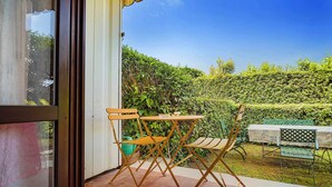 A patio with a table and chairs, a green chair, and a table with a white tablecloth. - Residence Moky D14 - pool, private garden, garage (Lazise)