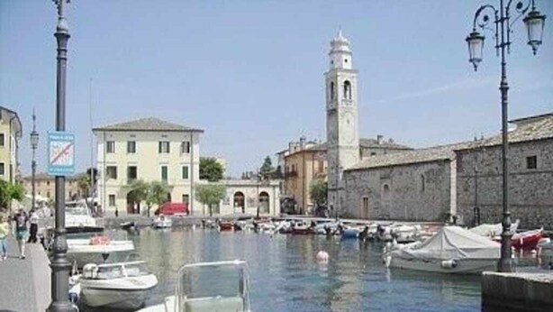 A marina with boats docked, a tower, and buildings along the waterfront. - Residence Moky D14 - pool, private garden, garage (Lazise)