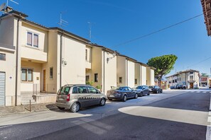 Straßenansicht mit parkenden Autos, einem Gebäude mit Balkon und einem Baum.