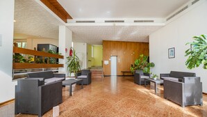 A modern lobby with a marble floor, grey wicker furniture, and potted plants.