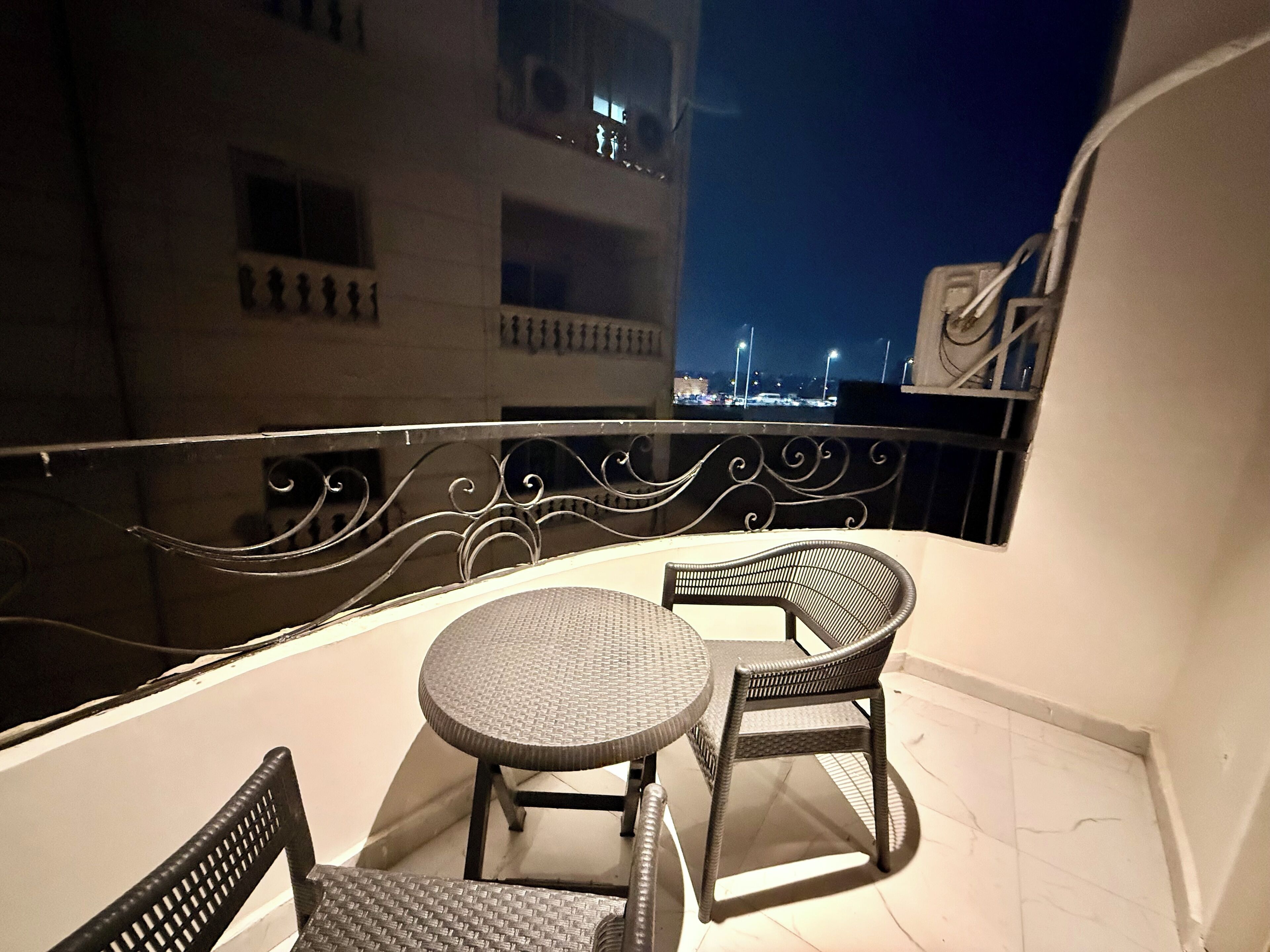 Un balcone con due sedie in vimini e un tavolino rotondo, con vista sulla città illuminata di notte.