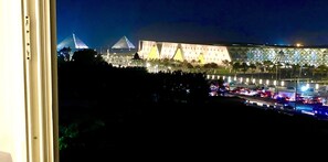 A nighttime view of a large, illuminated building with a pyramid-like structure in the background.