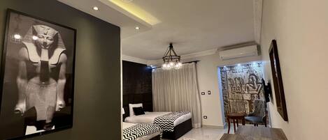 A modern hotel room with a bed, a desk, and a chair. There is a wall-mounted TV and a decorative wall piece.