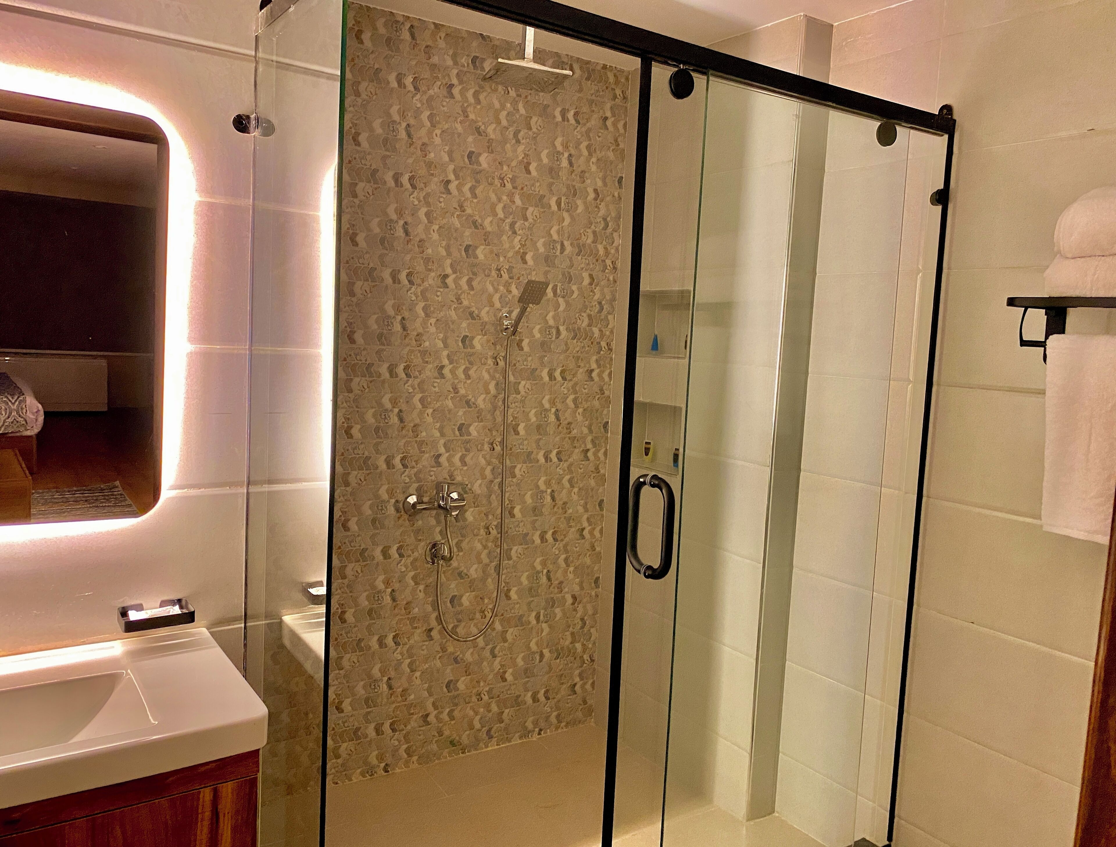 Uma casa de banho moderna com chuveiro de vidro, lavatório branco e espelho.