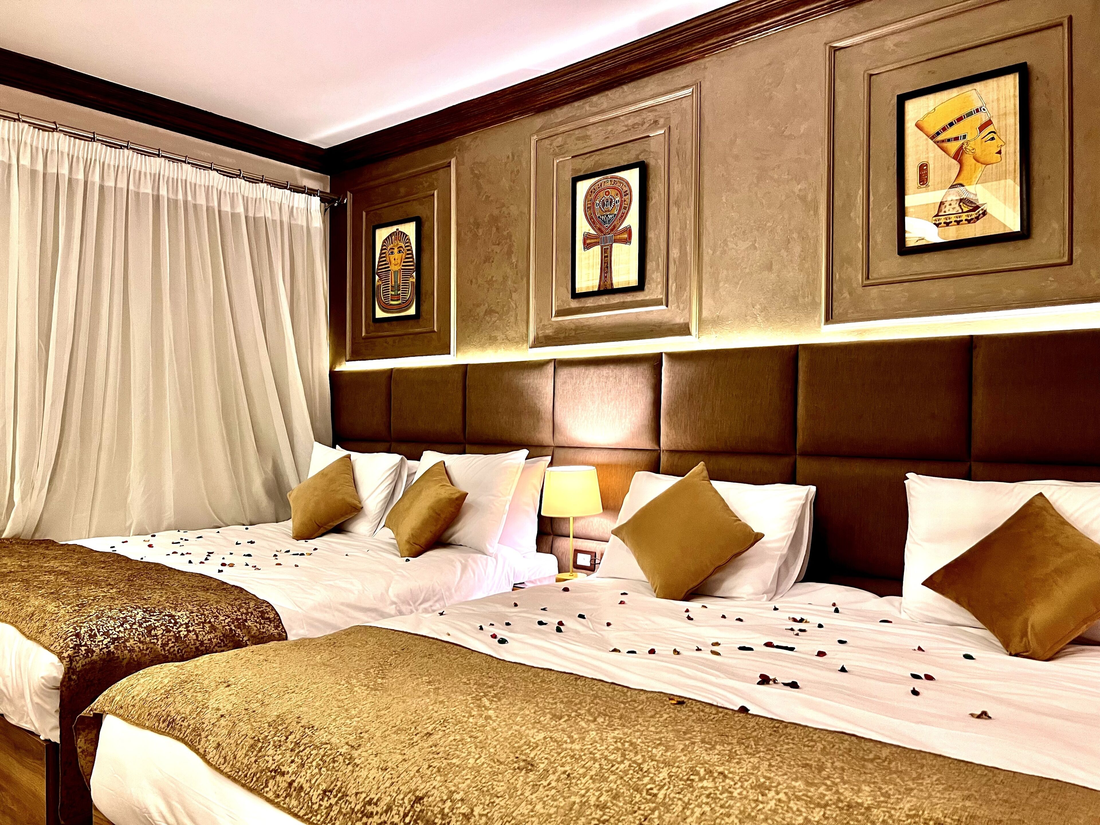 Habitación de hotel con dos camas, un ventanal grande con cortinas y cuadros colgados en la pared.