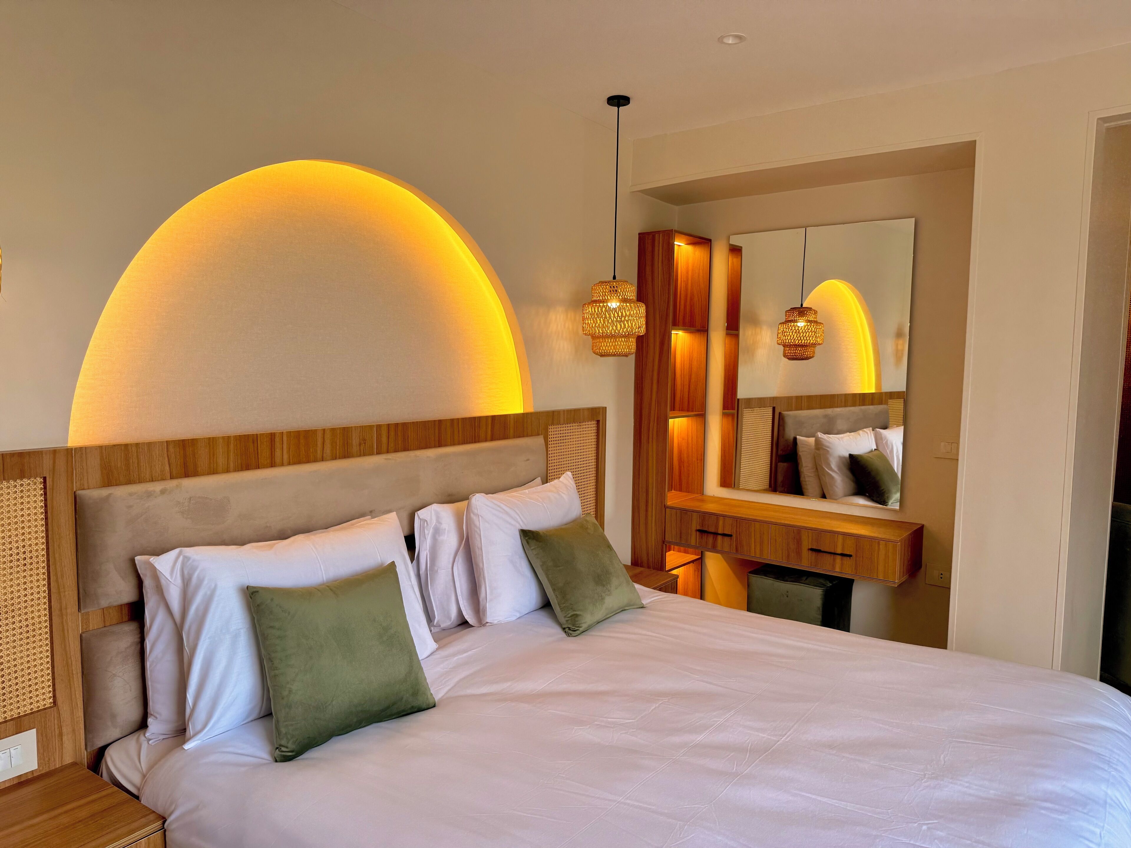 A hotel room with a large bed, wooden headboard, and a mirror above the vanity.